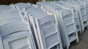 A section of white folding chairs standing up against a wall. 